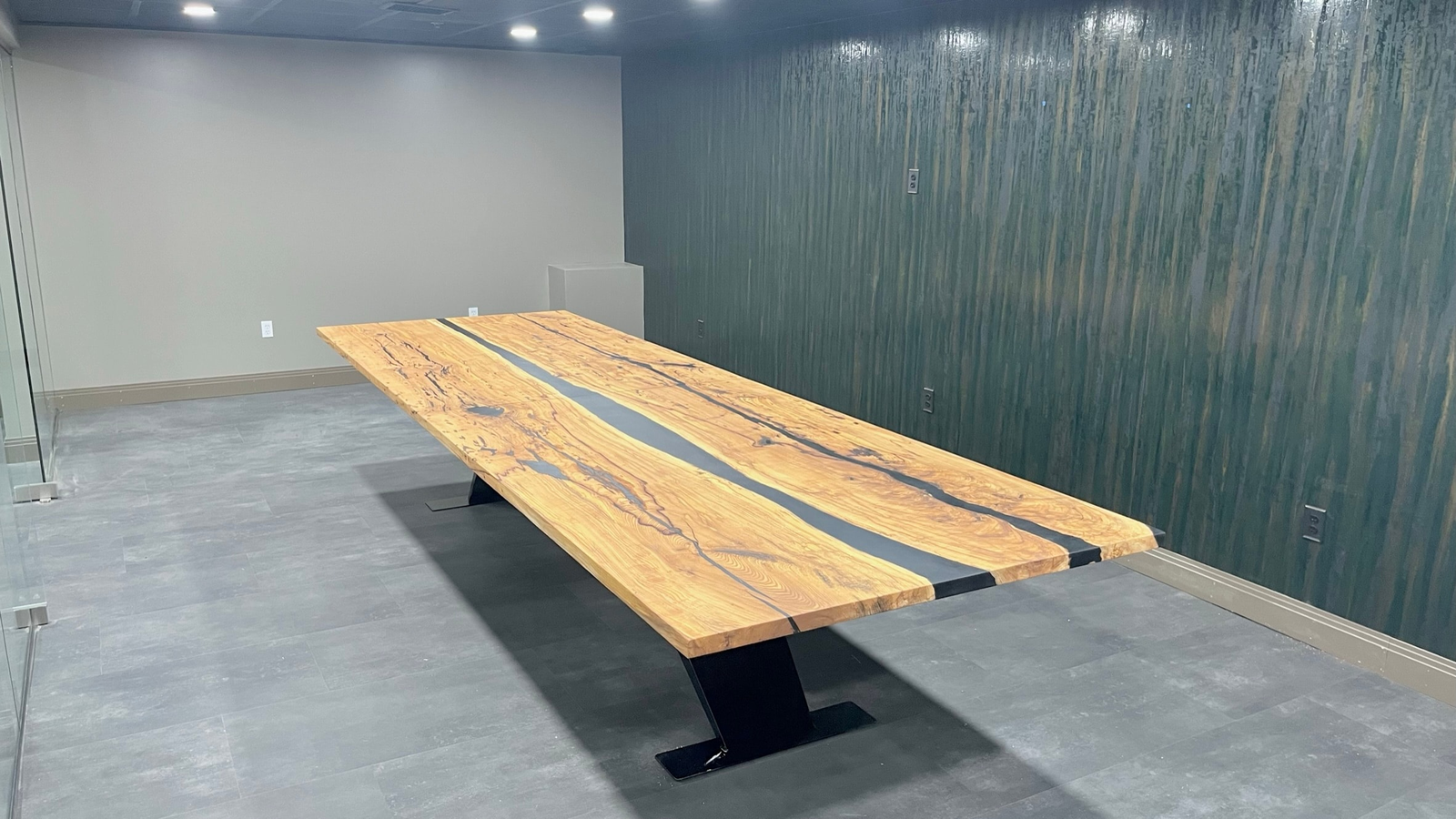 A long spalted conference table with a black river through the top, on a black steel base, installed in an office with dark wood-slat walls. Built by Robert Russell Designs.
