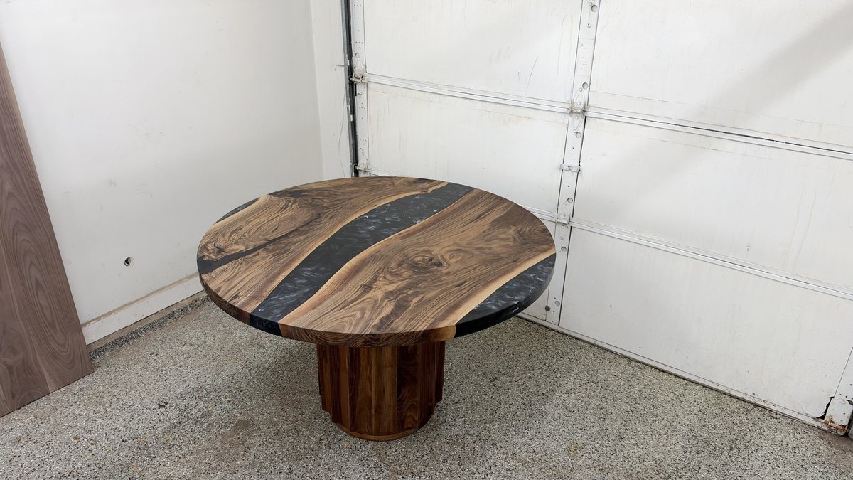 A round walnut table with a black river through the top, on a fluted walnut drum base, in Rob's shop