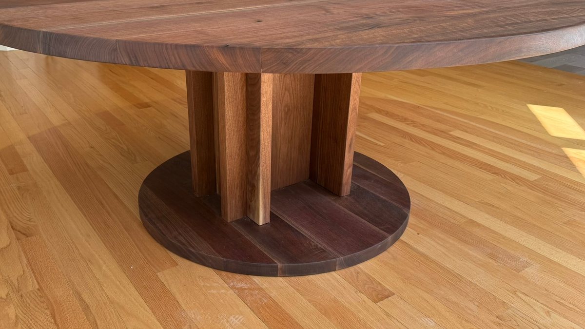 A round solid walnut table on a pedestal of boards set in a cross, standing on a round plinth