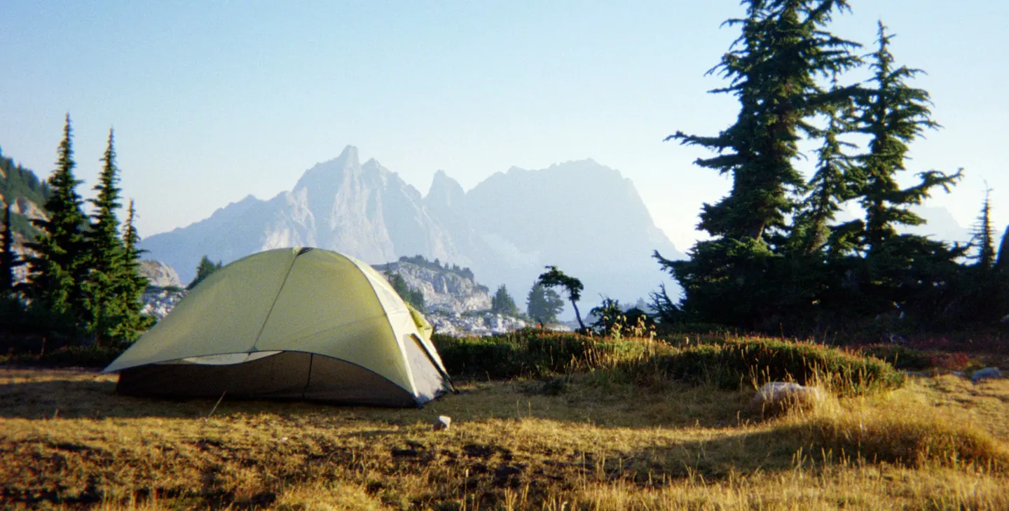 A backcountry tent pitched on a golden alpine meadow below granite peaks in the Alpine Lakes Wilderness, Washington.