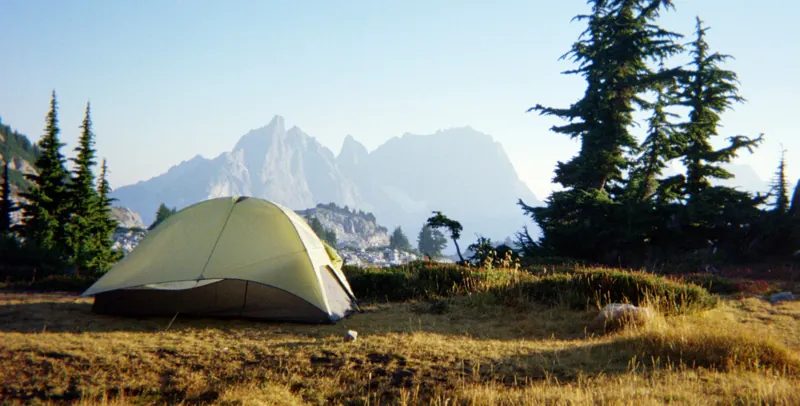 A backcountry tent pitched on a golden alpine meadow below granite peaks in the Alpine Lakes Wilderness, Washington.
