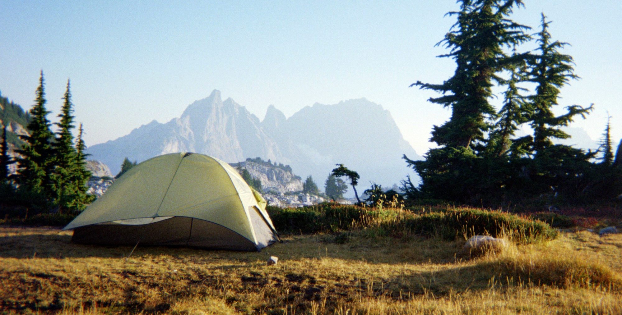 A backcountry tent pitched on a golden alpine meadow below granite peaks in the Alpine Lakes Wilderness, Washington.