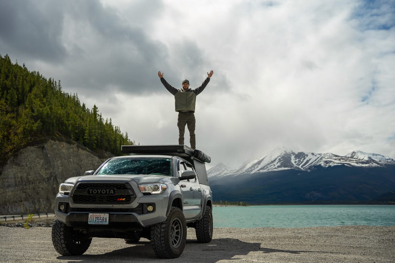 Conner Crowe standing on a Tacoma above a glacial mountain lake.